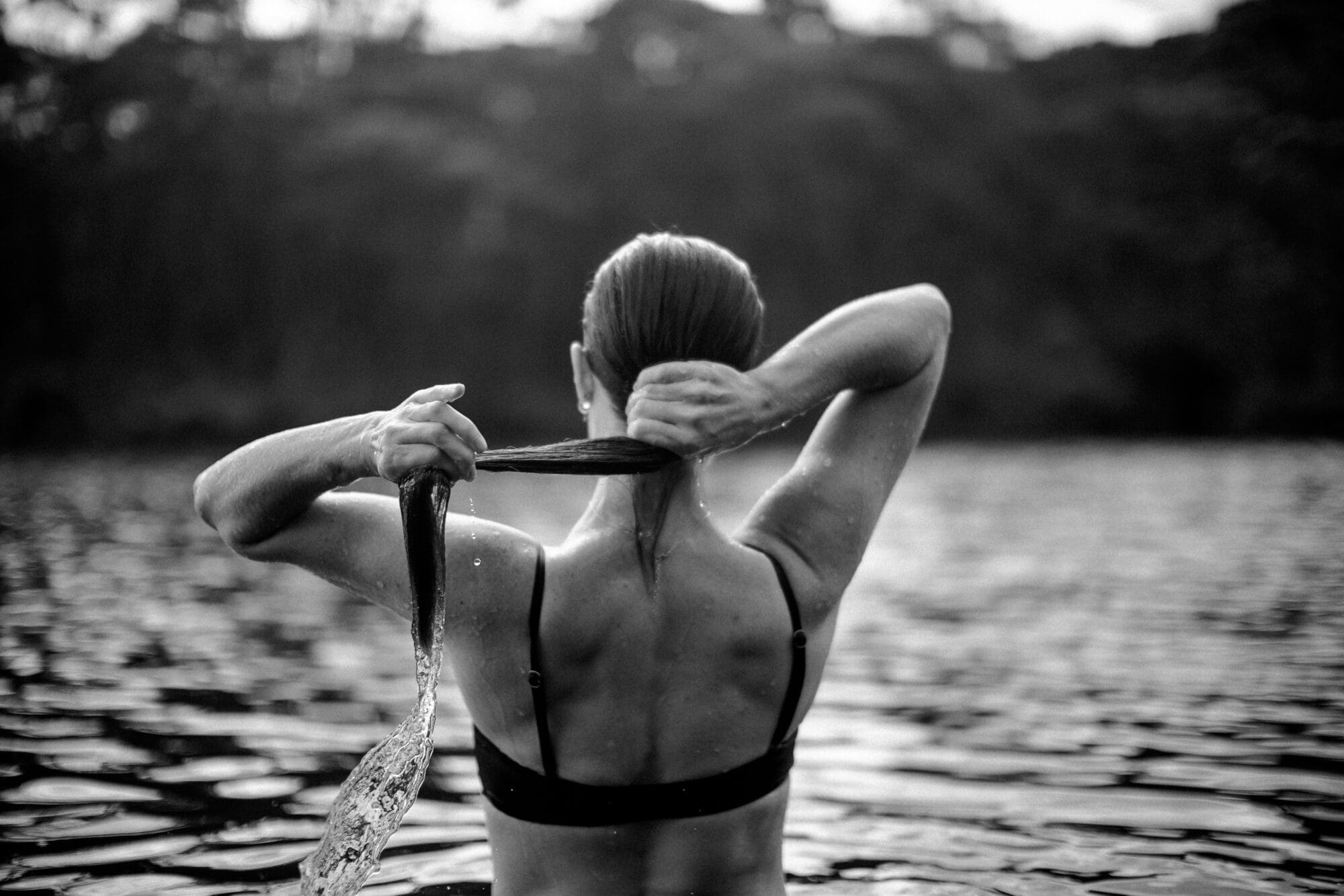 Black and white photo of a woman from behind, wringing her wet hair in water.